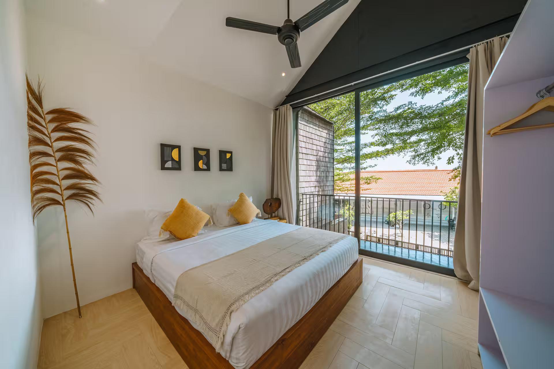 Bedroom at Villa RIZR with ochre cushions, a dried palm frond and a balcony over the trees