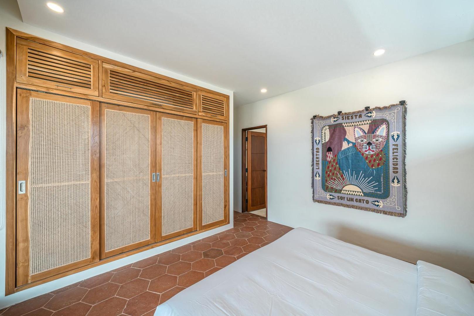 Second bedroom with a wall of cane-fronted wardrobes and a woven tapestry above the bed