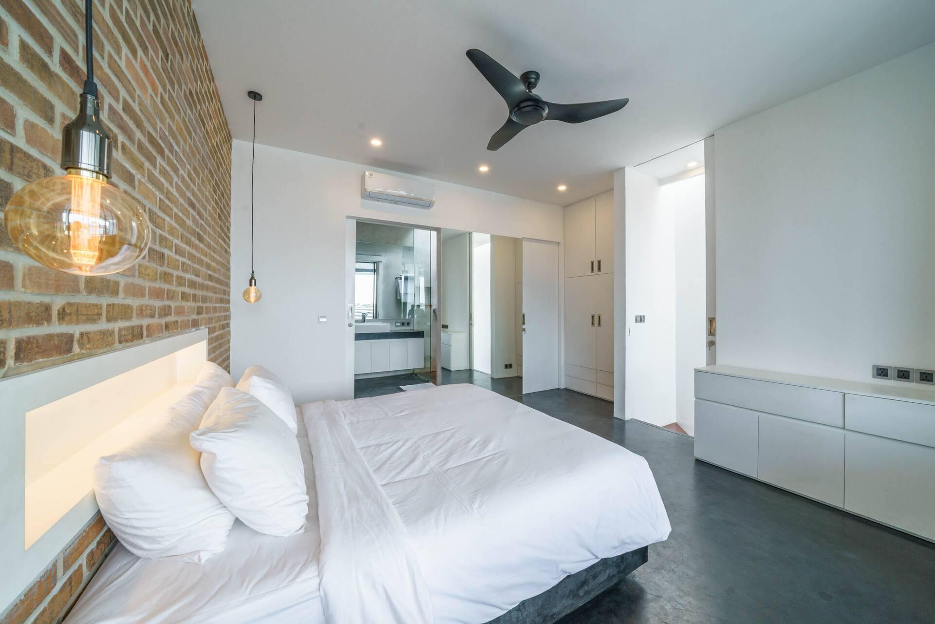 King bed against the brick wall, the en-suite doorway open at the far end