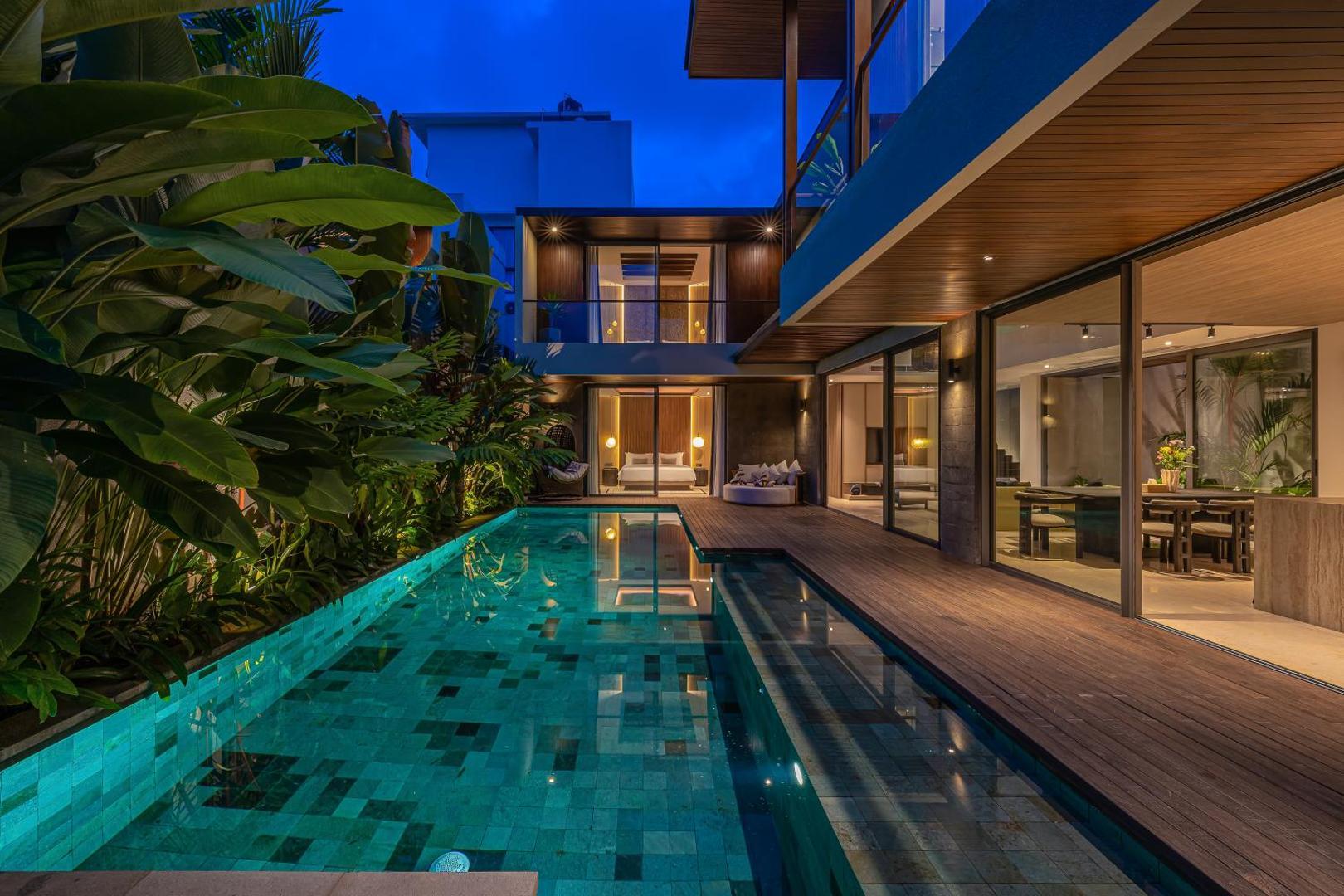 The pool lit at dusk, mosaic tile glowing beside the hardwood deck