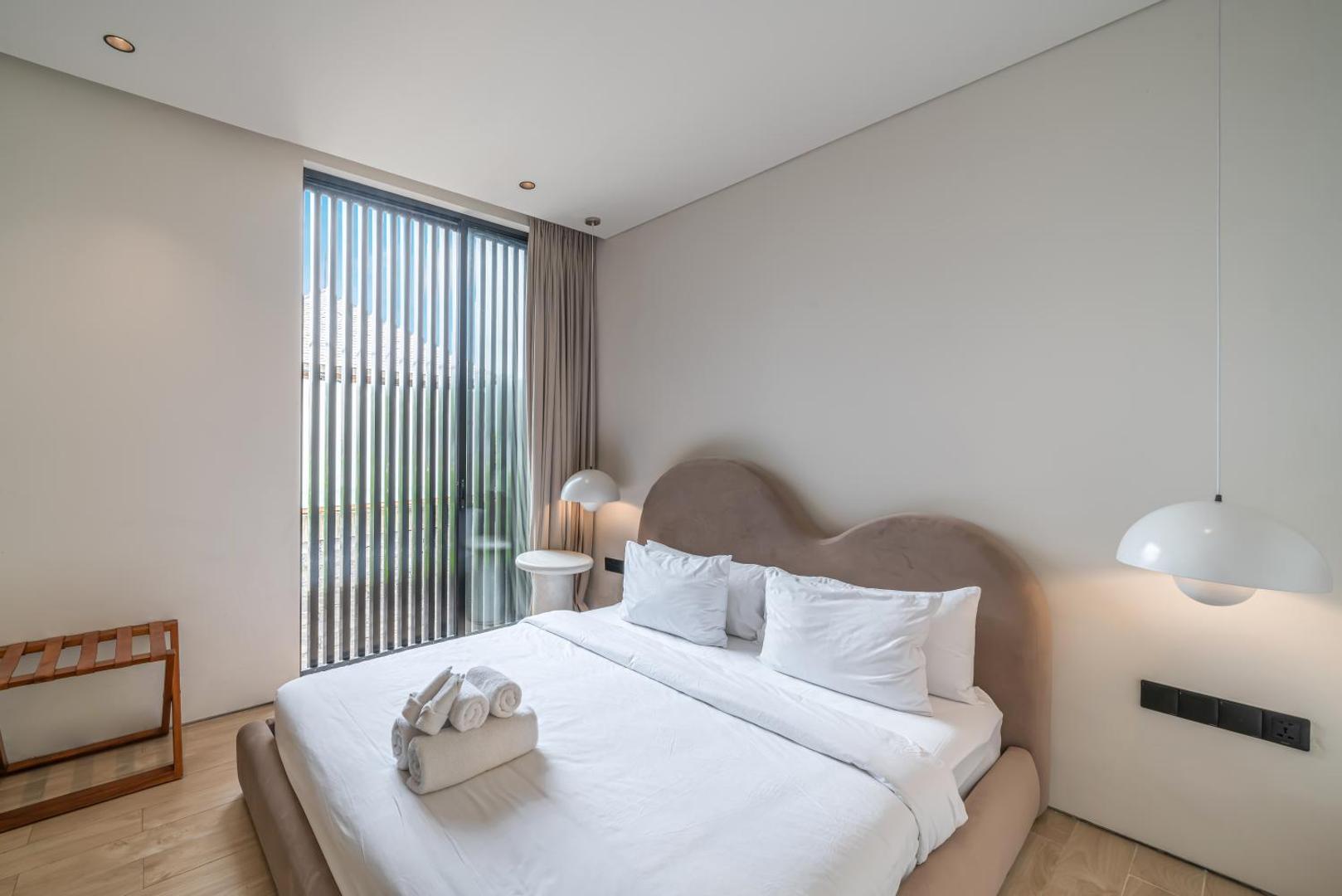 Bedroom with a curved upholstered headboard and a tall slatted window onto the garden