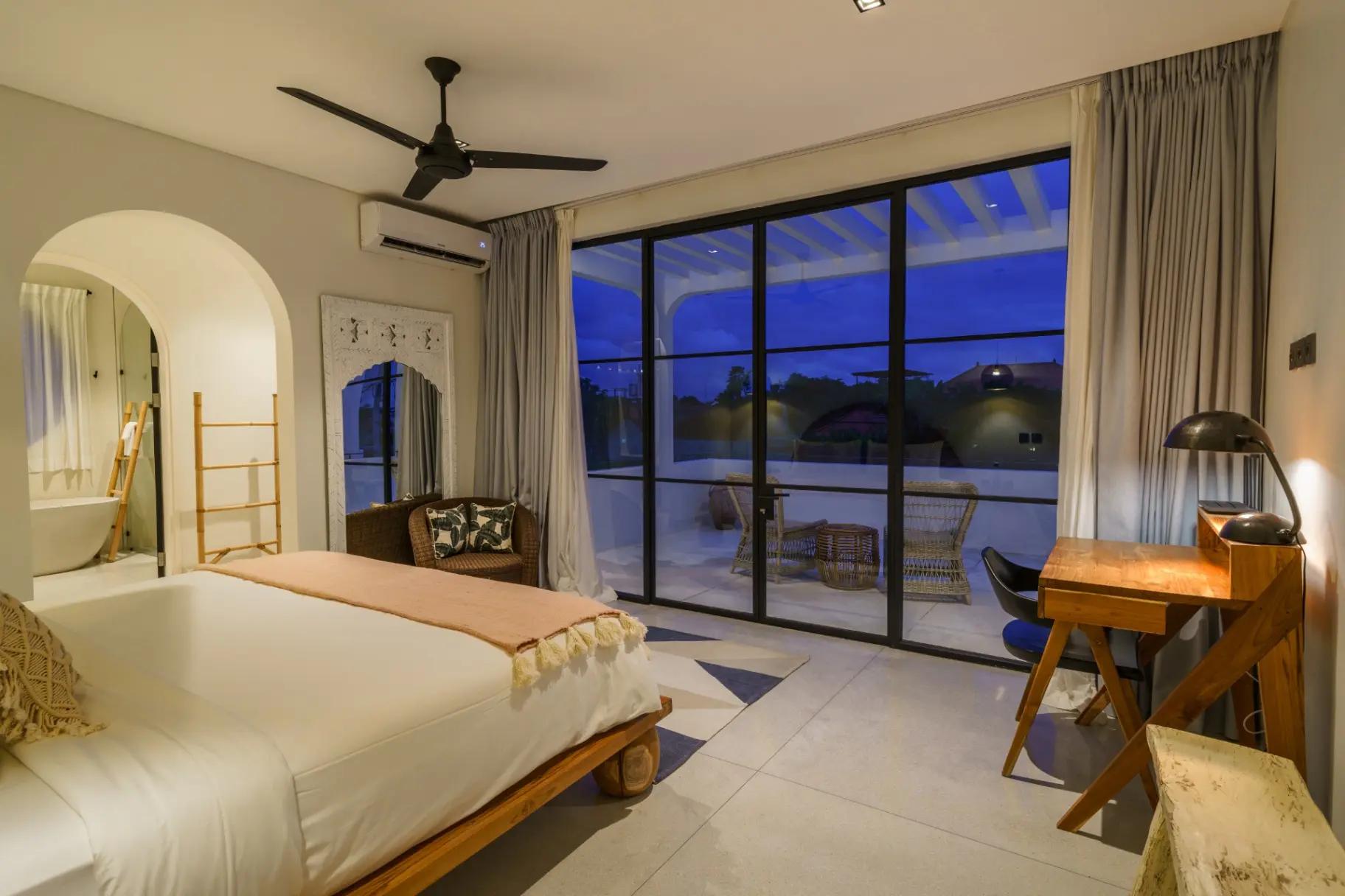 Bedroom at dusk with sliding glass to the terrace, timber desk and an arched alcove
