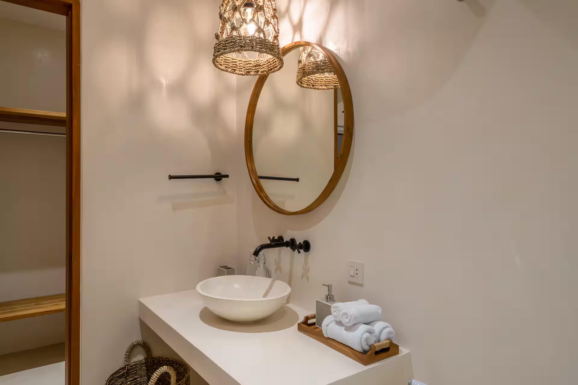 En-suite bathroom with a stone vessel basin, black tapware and a round timber-framed mirror