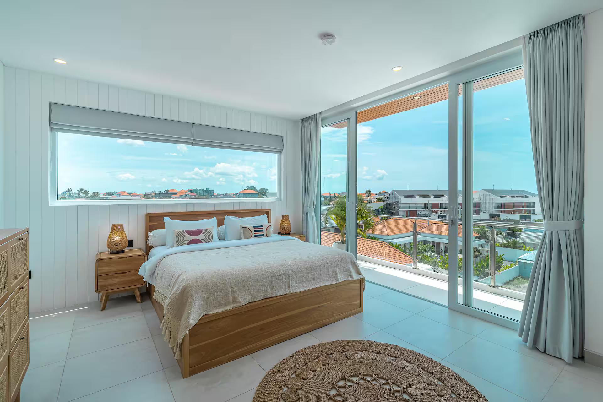 Bedroom opening to a balcony above the tiled roofs, curtains drawn back from the glass
