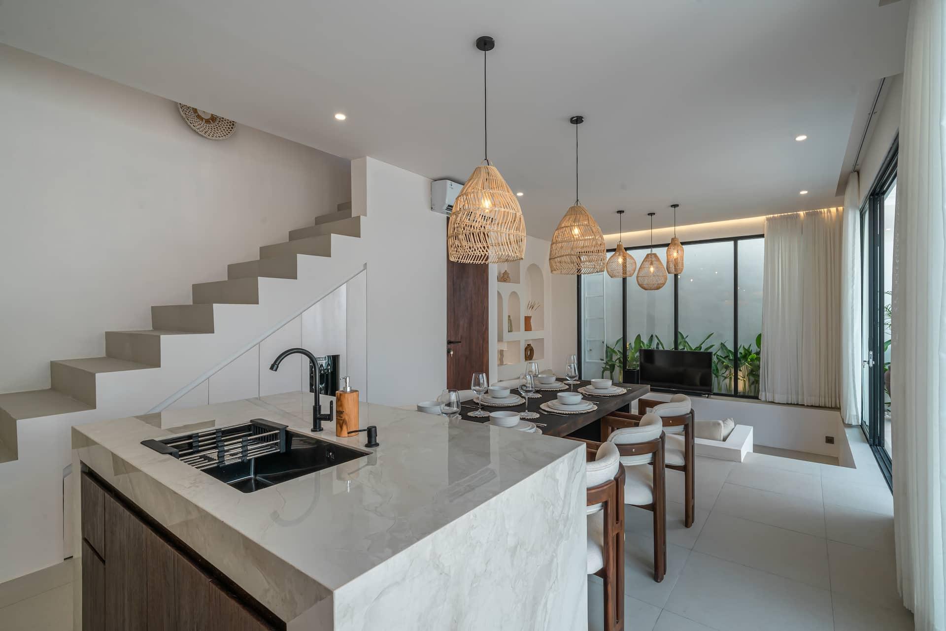 Marble kitchen island with a black sink and brass mixer, stair rising alongside