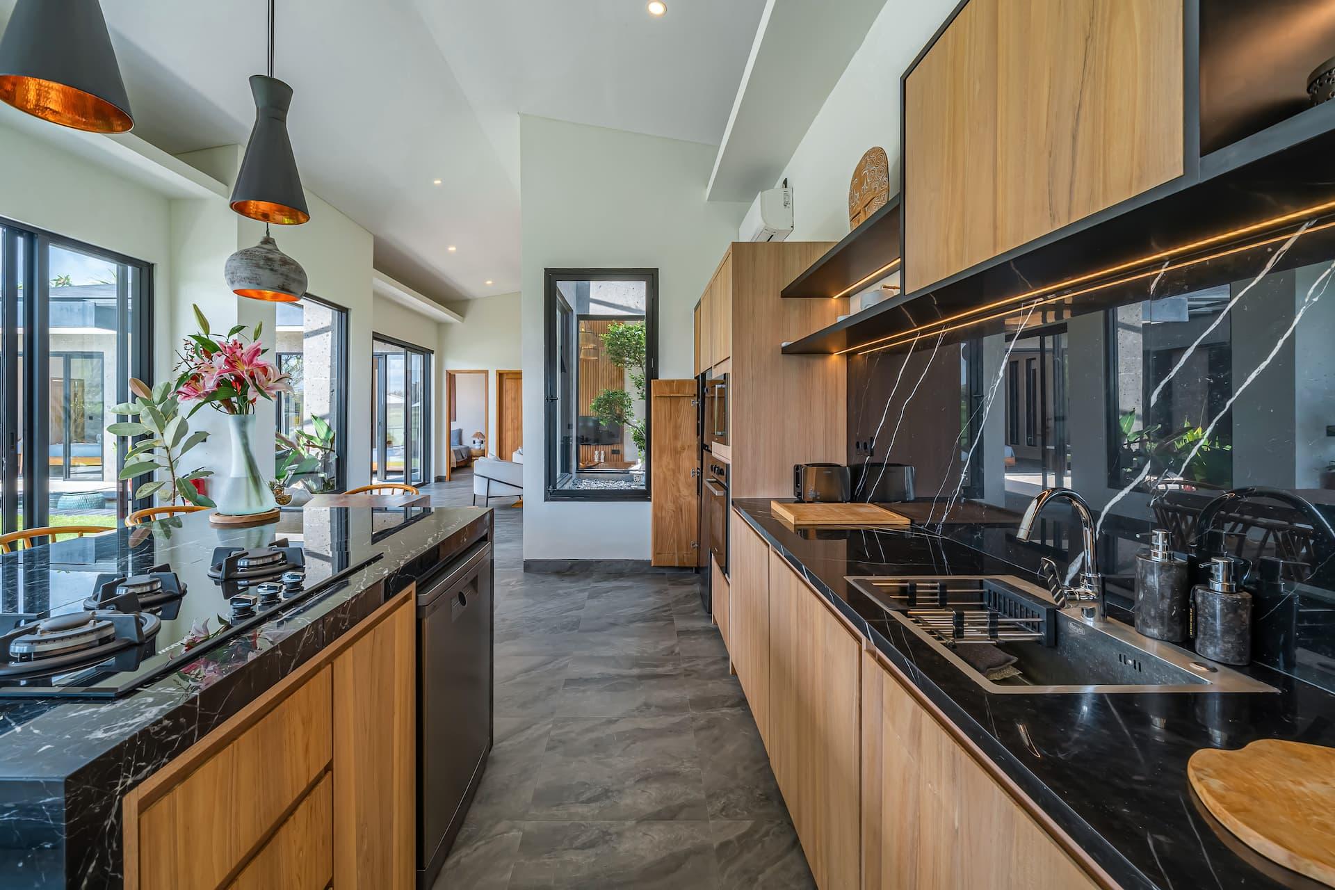 Black marble kitchen island with integrated hob, pale timber cabinetry and copper pendants