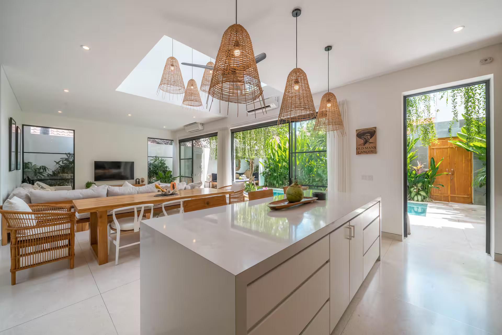 A white kitchen island under a run of oversized woven-rattan pendants