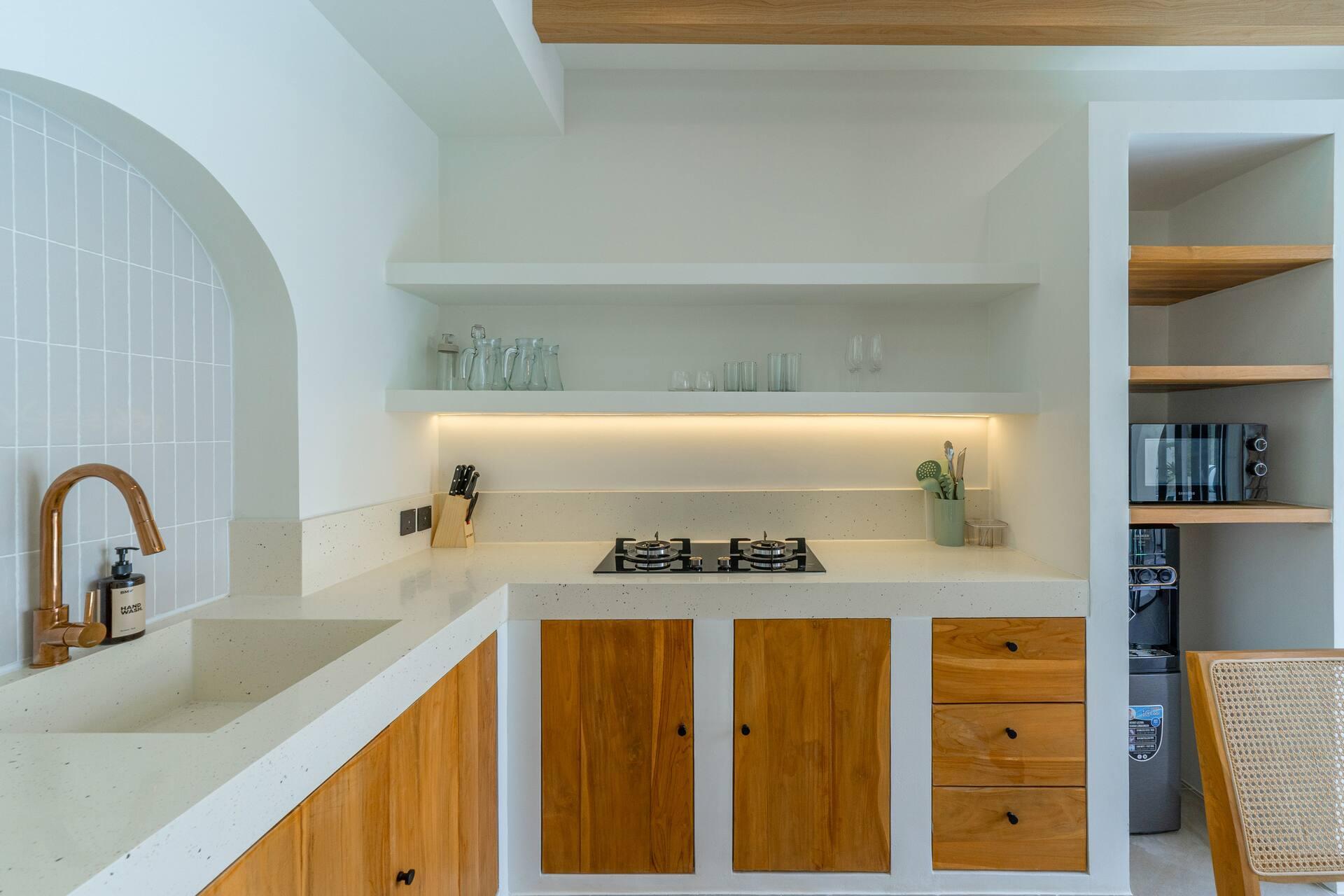 Villa Solmea's kitchen with timber cabinets, a gas hob, brass tap and open shelving under soft lighting