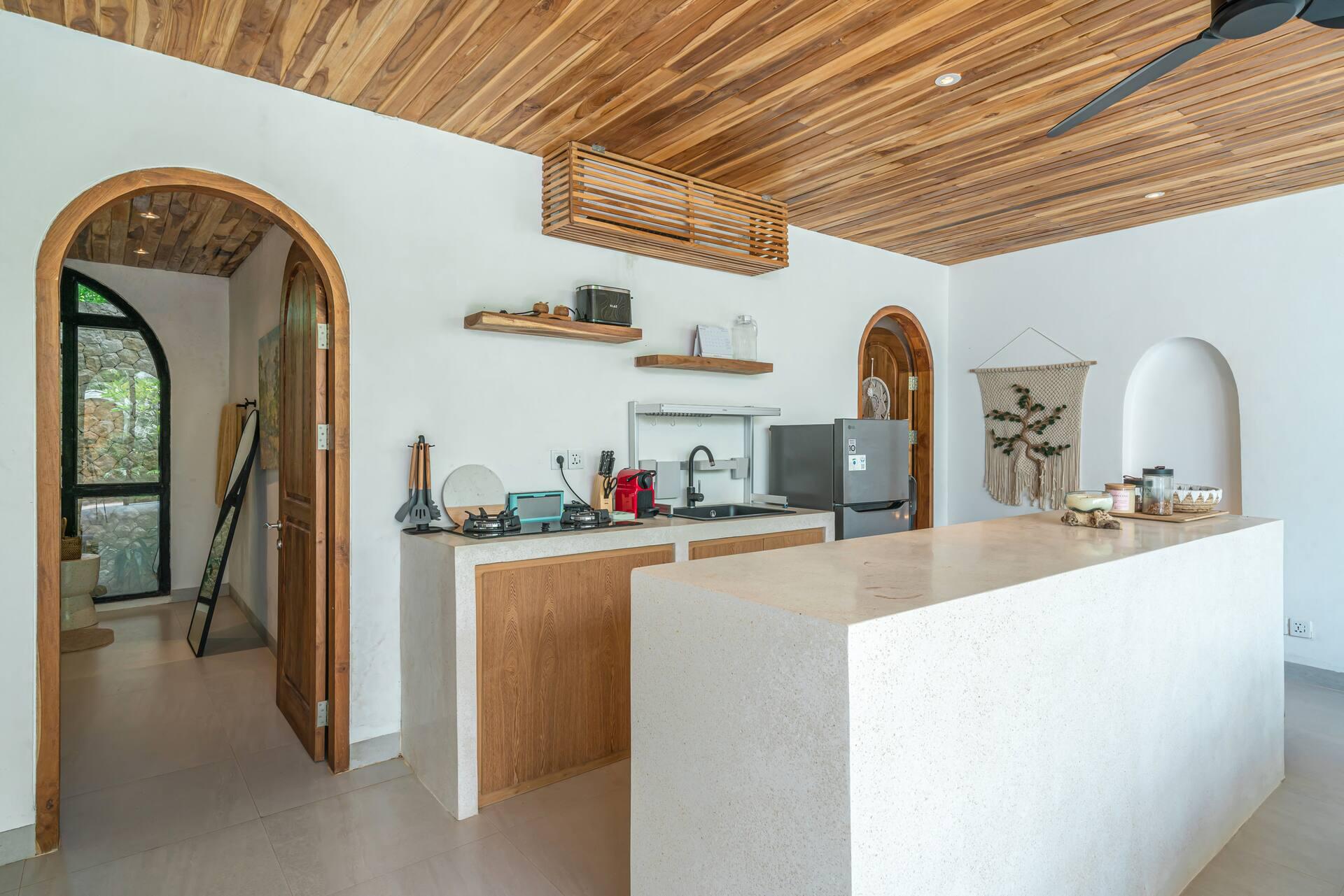 Kitchen with a white island, timber cabinetry and an arched timber doorway at Villa Dharma