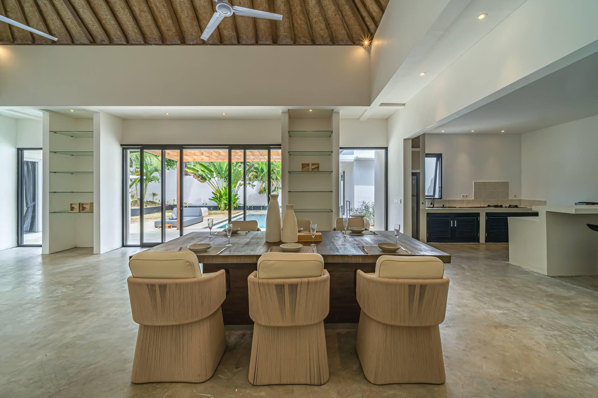 Long timber dining table with woven chairs, looking through glass doors to the pool terrace