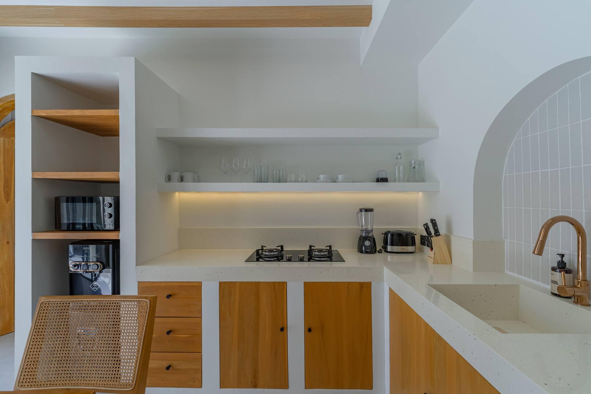 Kitchen with timber cabinet fronts, a gas hob, brass tap and open shelves under warm strip lighting