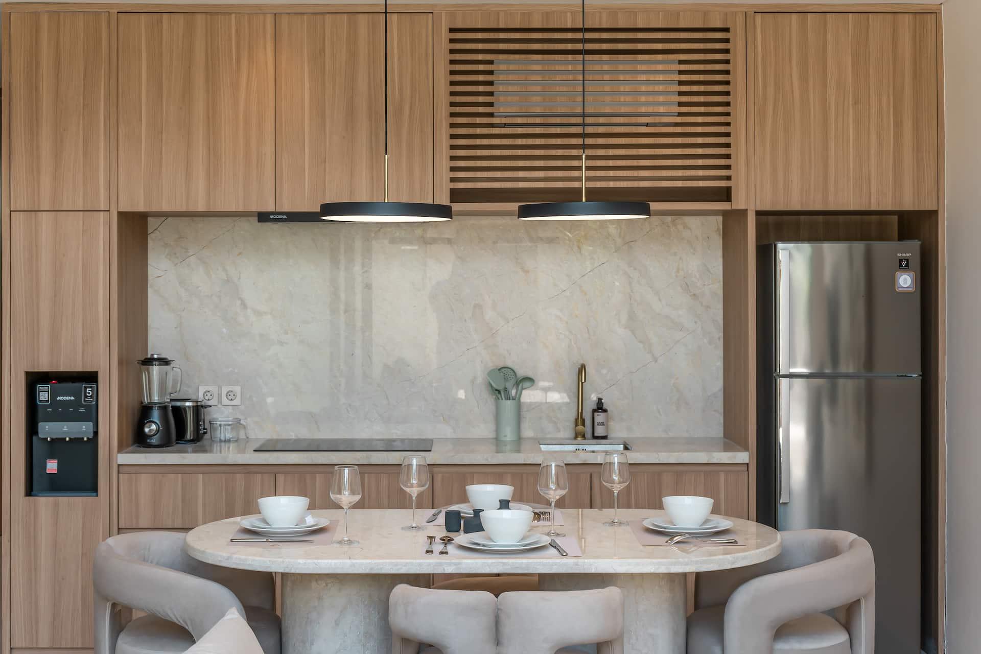 Kitchen in pale timber with a stone splashback, built-in oven, tall fridge and an oval dining table