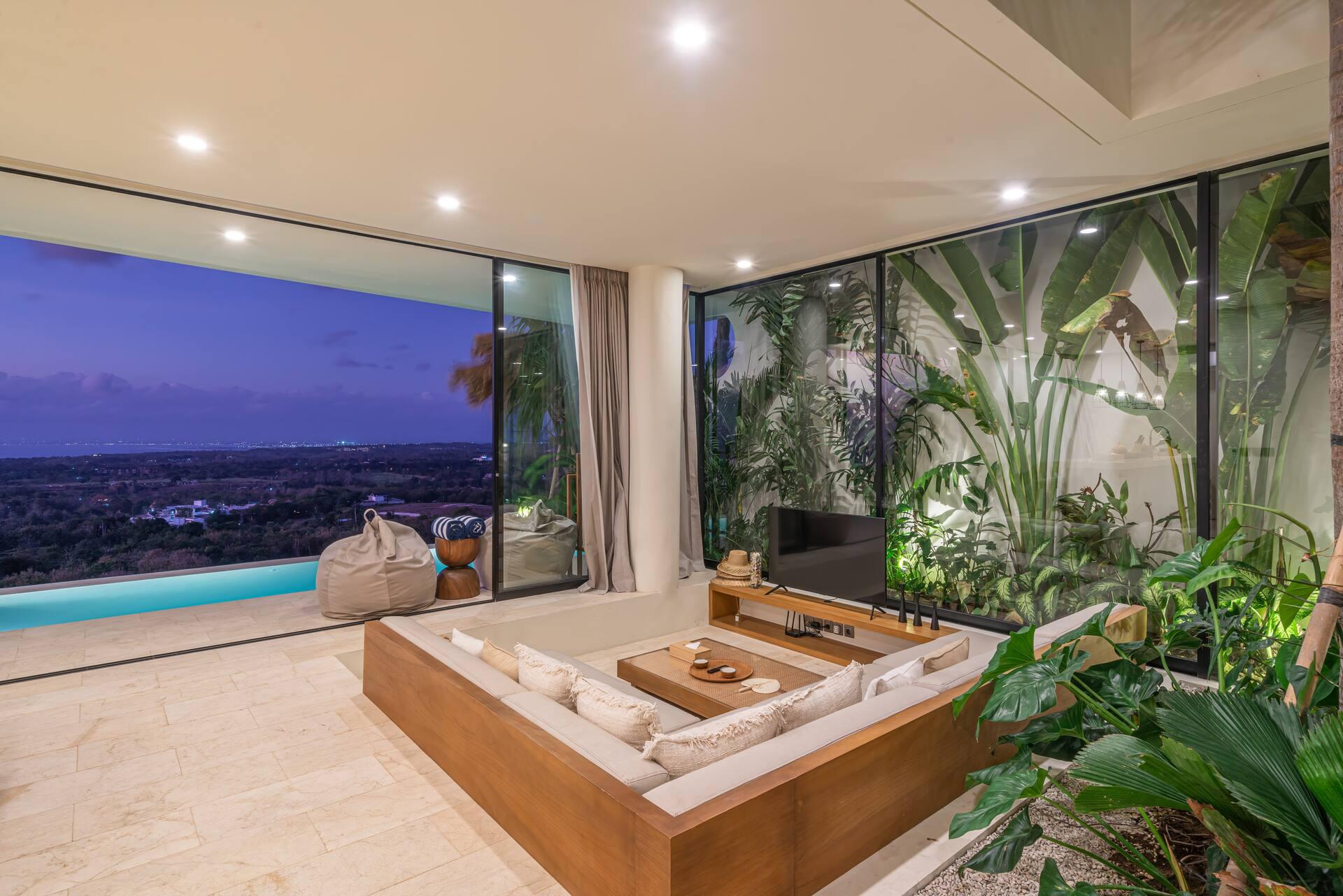 Sunken lounge at dusk, with the indoor tropical garden on one side and the lit pool beyond
