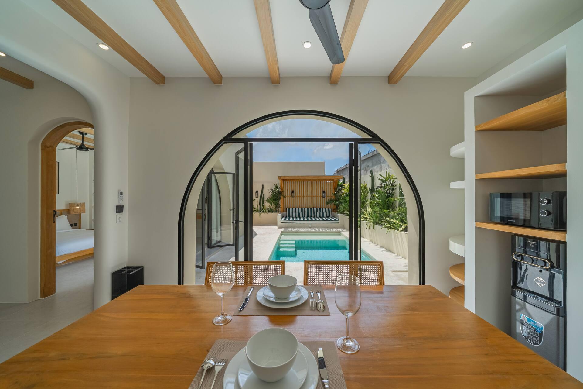Dining table laid for two, looking through an arched doorway to the pool and pergola