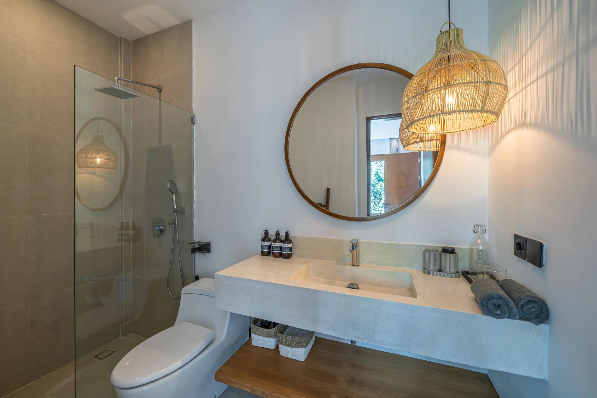 En-suite with a walk-in glass shower, round timber mirror and a cast-concrete basin